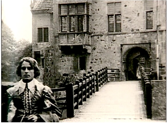 Film still from Der Knabe in Blau: a young man in period costume stands before the moated castle Burg Vischering